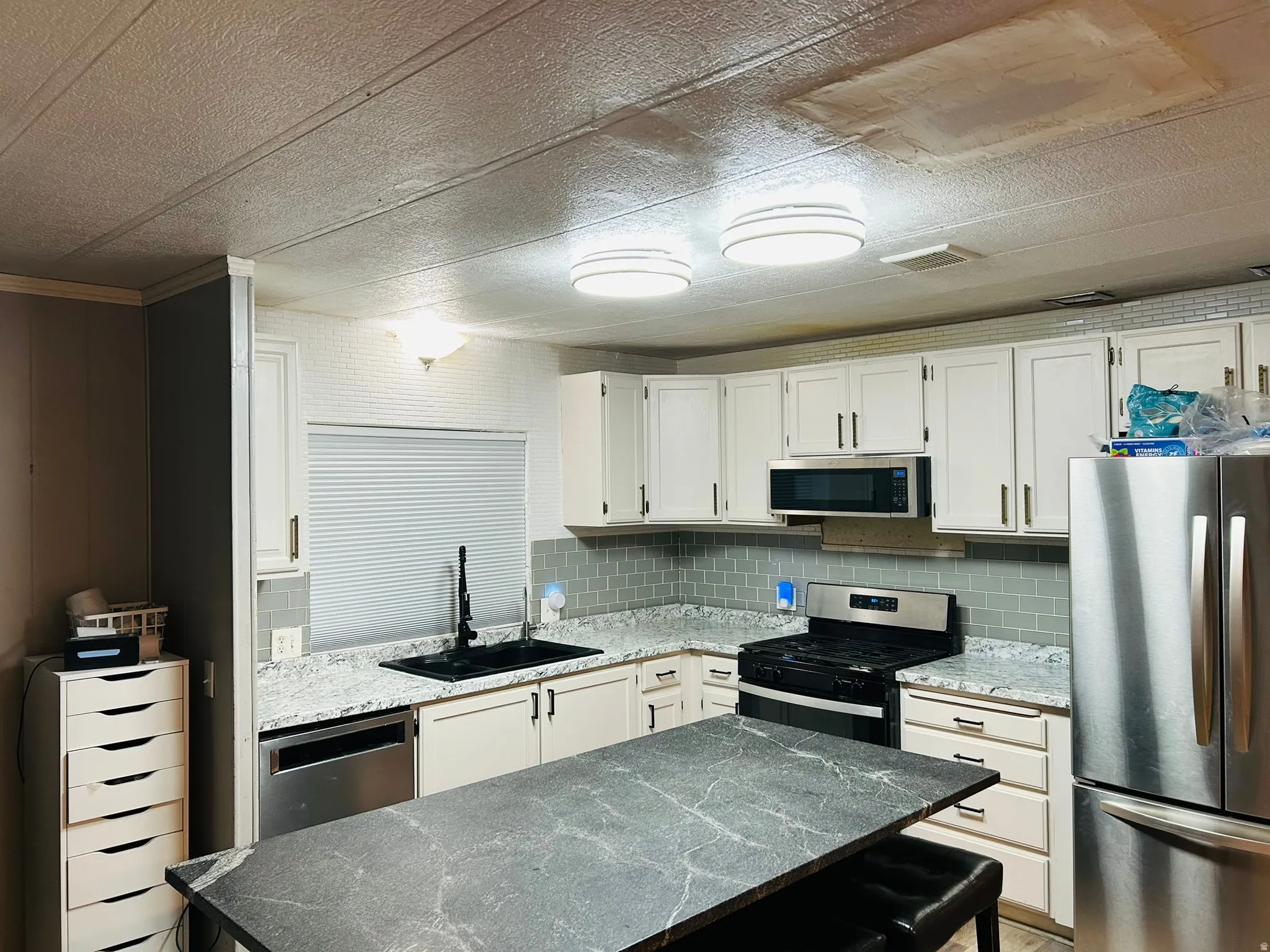 Kitchen featuring white cabinetry, grey subway tile backsplash, white countertops with grey flecks, and stainless steel appliances