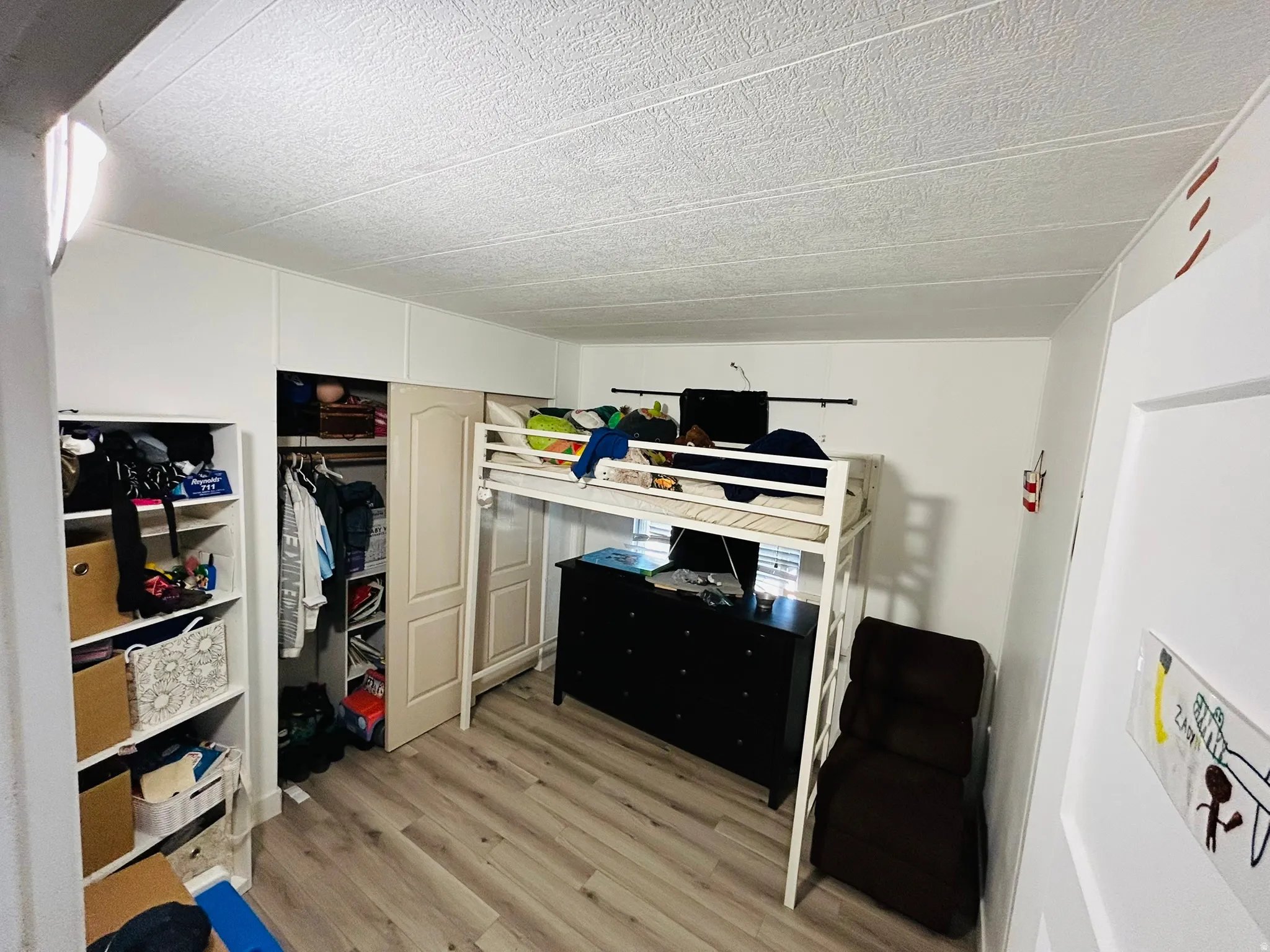 Bright room featuring light wood-finish flooring, a bi-fold closet door, and a textured white ceiling