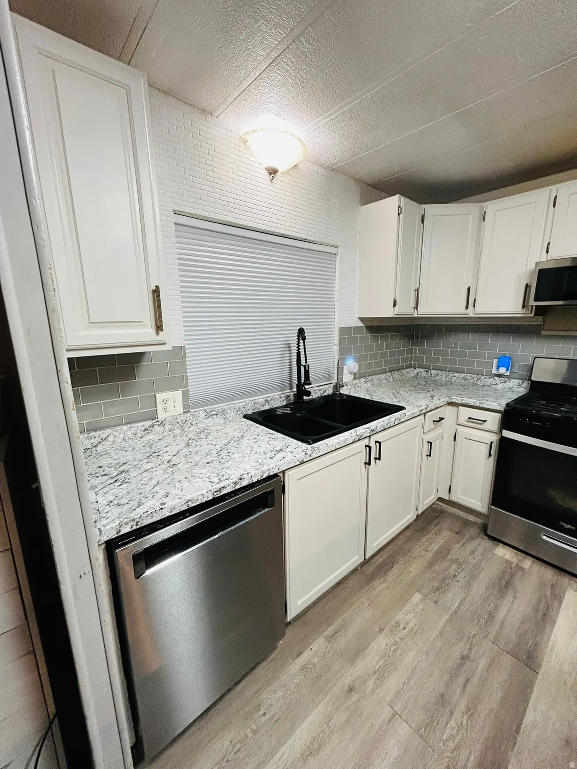 Kitchen featuring white cabinetry with dark hardware, a double basin black sink with a matte black faucet, and light-toned countertops