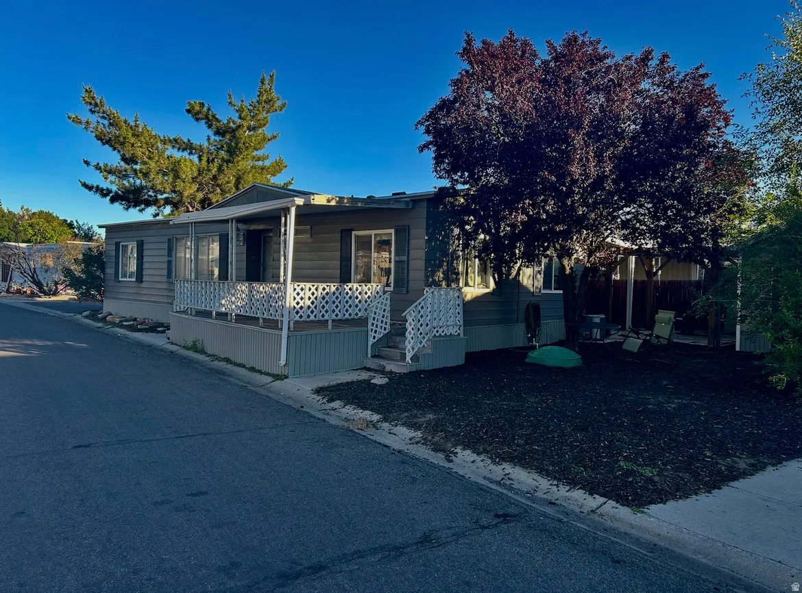 Manufactured home featuring horizontal siding, a covered porch with lattice railing, and a mature tree providing shade