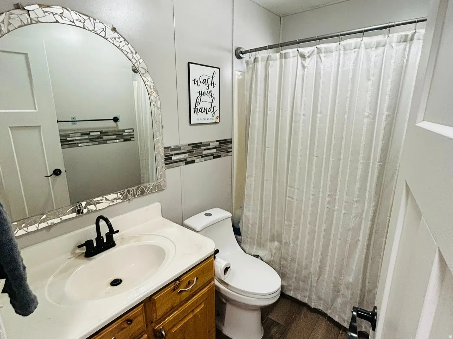 Bathroom featuring a wood-finish vanity with an integrated sink and matte black faucet, mosaic-tiled mirror, and wood-look flooring