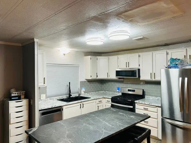 Kitchen featuring white cabinetry, grey subway tile backsplash, white countertops with grey flecks, and stainless steel appliances
