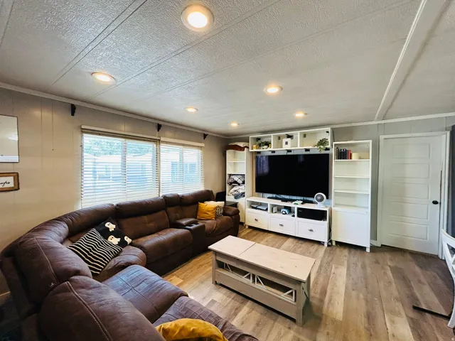 Living area featuring wood-finish flooring, recessed ceiling lights, and multiple windows with blinds