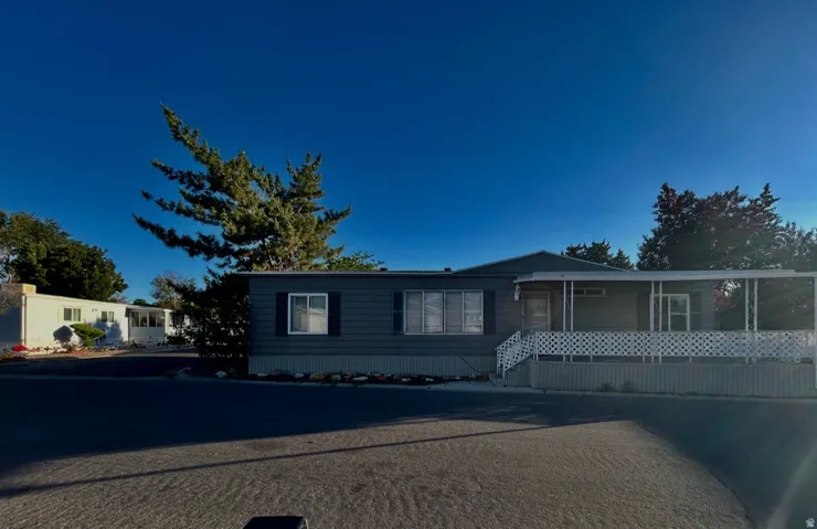 Single-story residence featuring blue siding with white trim, a covered front porch, white railing, and a mature evergreen tree