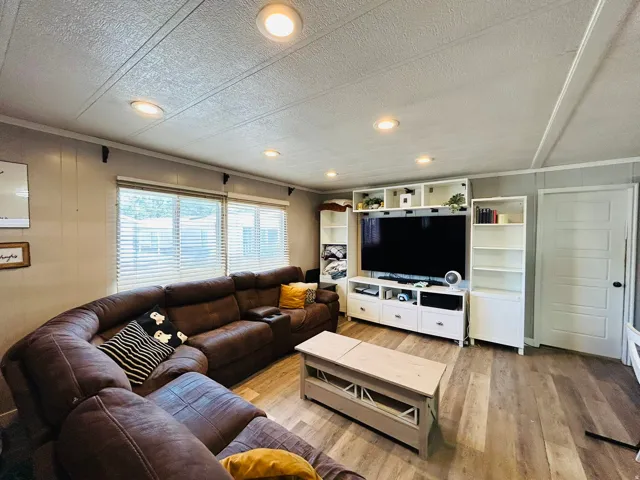 Living area with recessed ceiling lights, wood-finish flooring, multiple windows with blinds, and built-in white shelving units