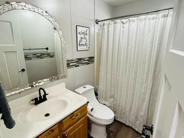 Bathroom featuring a wood-finish vanity with an integrated sink and matte black faucet, mosaic-tiled mirror, and wood-look flooring