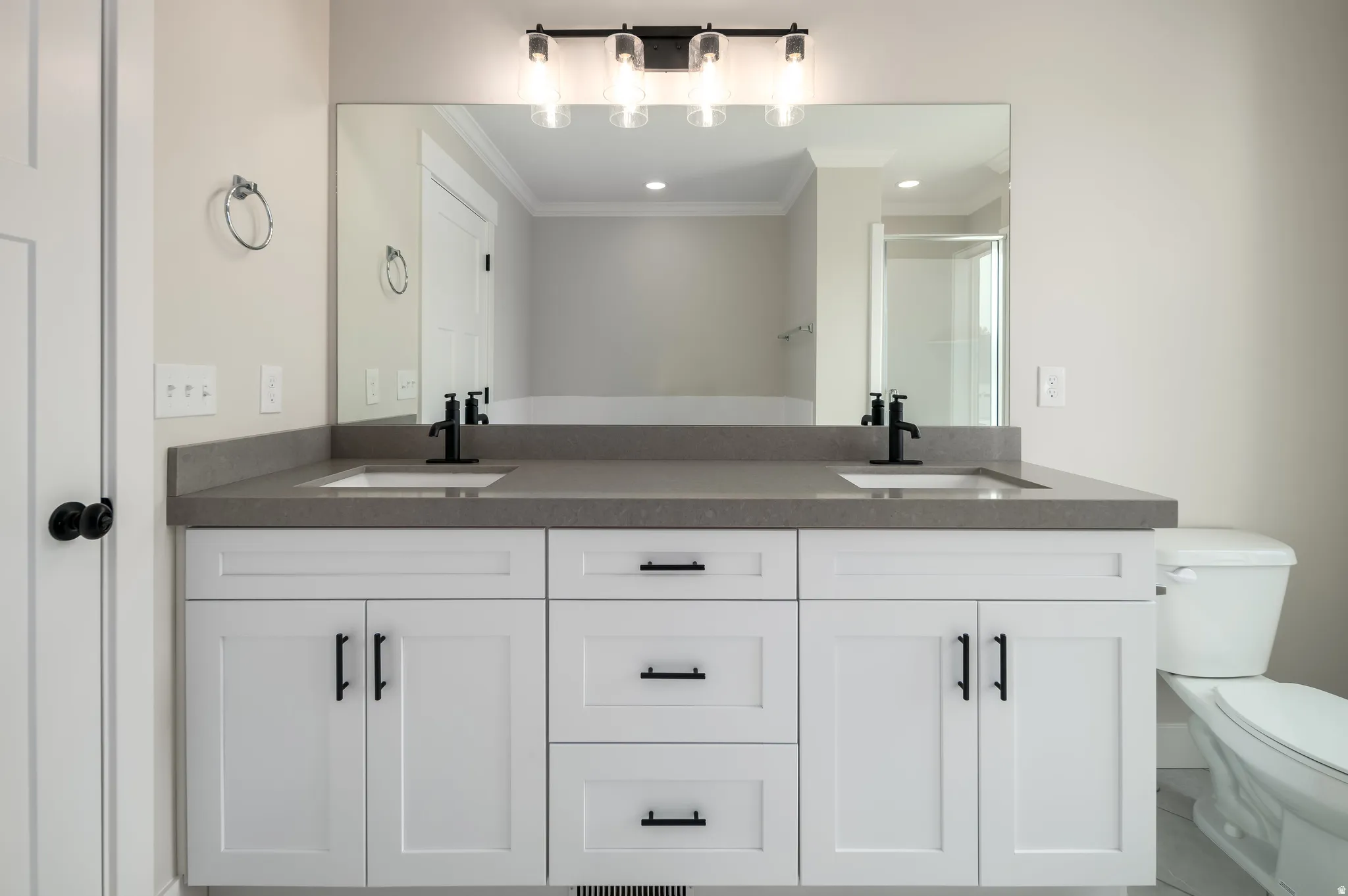 Dual white vanity featuring shaker-style cabinetry, matte black hardware, and a grey countertop with integrated sinks