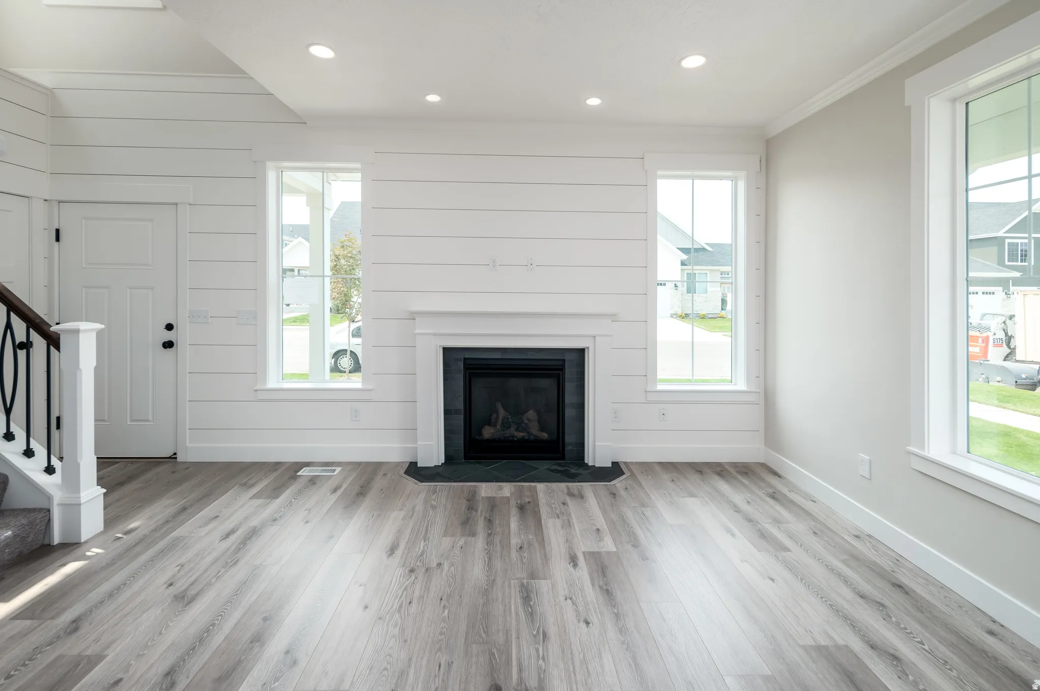 Living space featuring a shiplap accent wall, a white mantel fireplace with dark stone surround, and wood-finish flooring