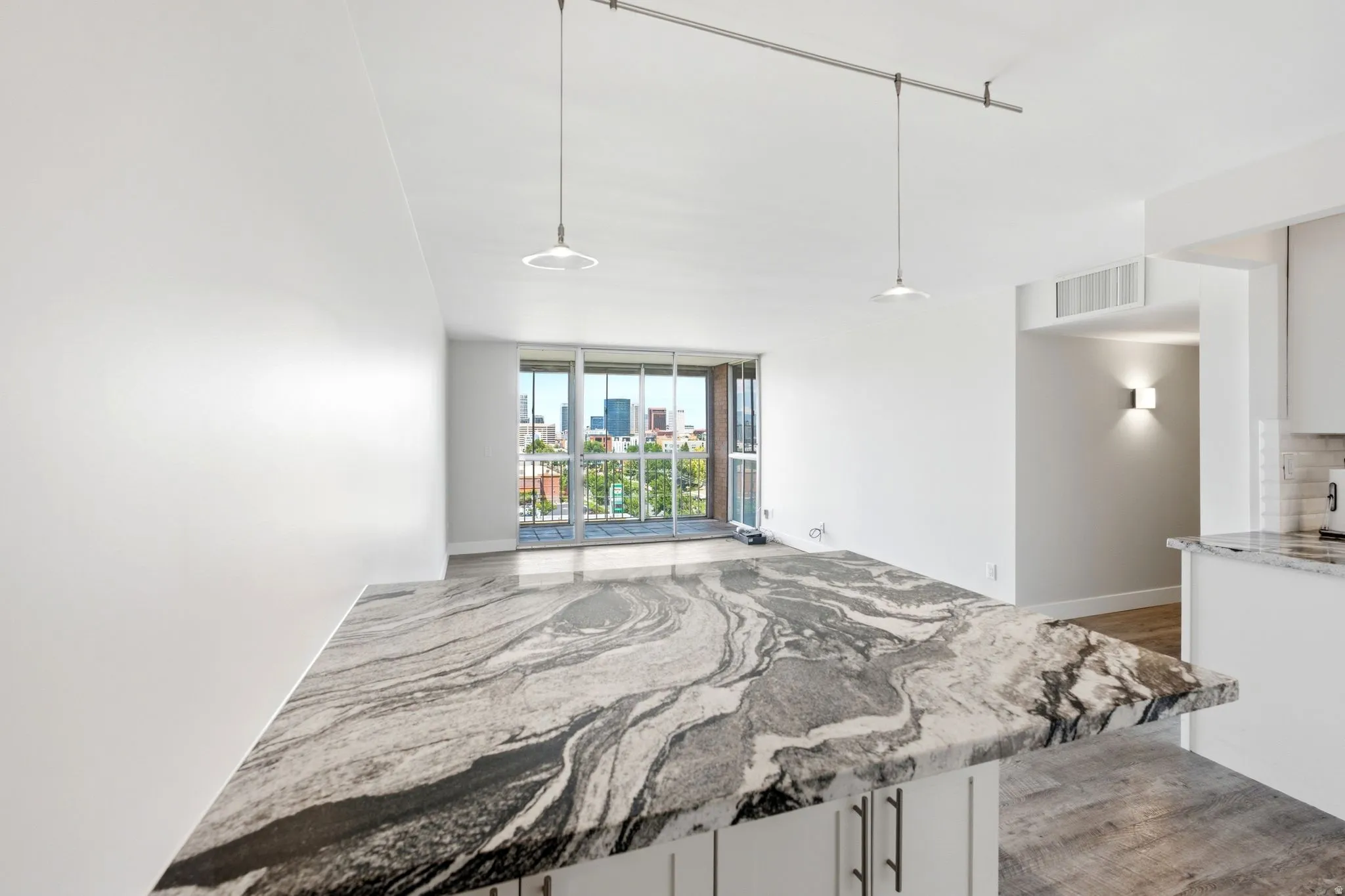 Spacious open-concept living area featuring an expansive kitchen island with a striking natural stone countertop, pendant lighting, and wood-finish flooring