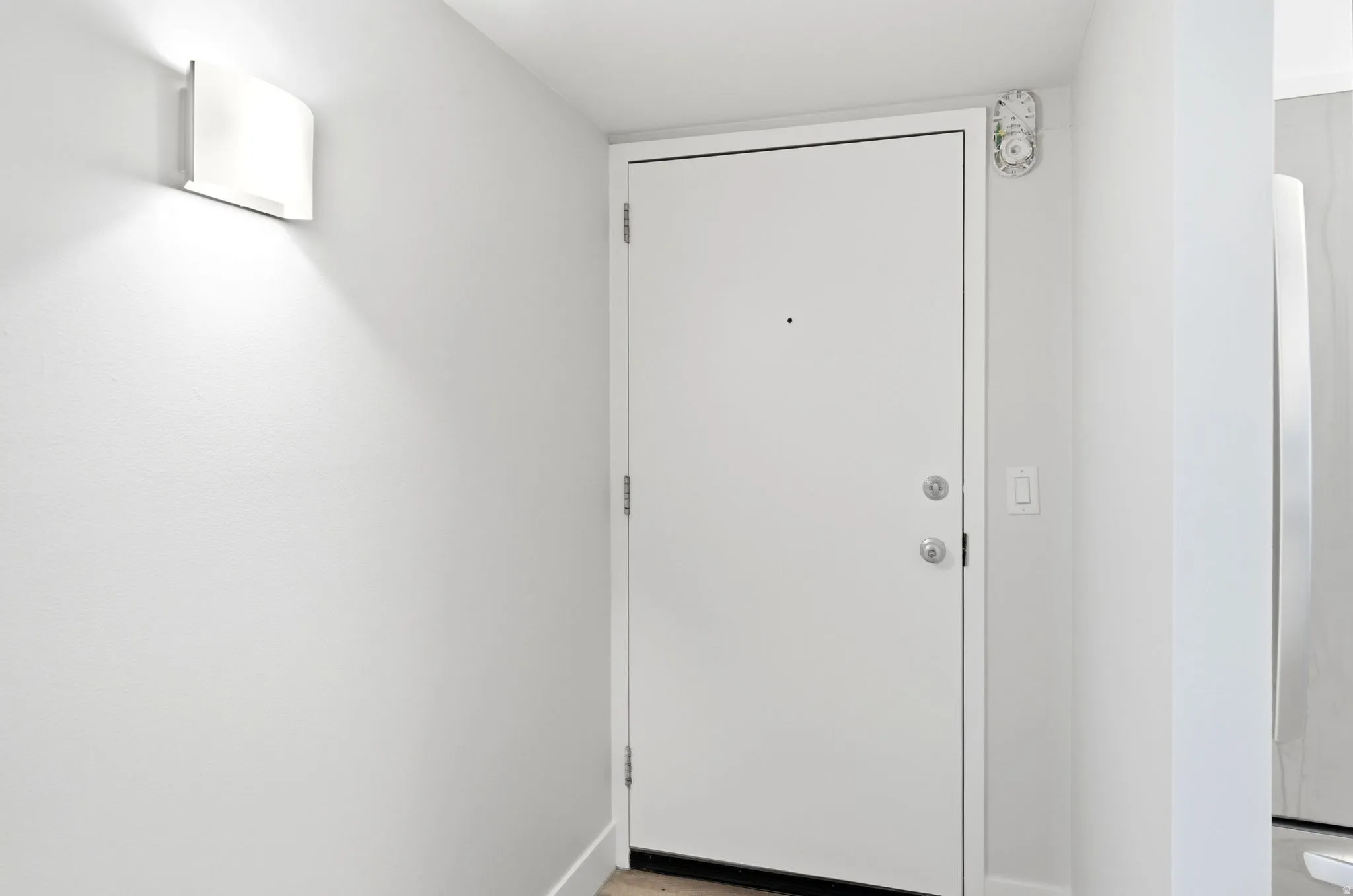 White entry door with satin nickel hardware and a wall-mounted sconce