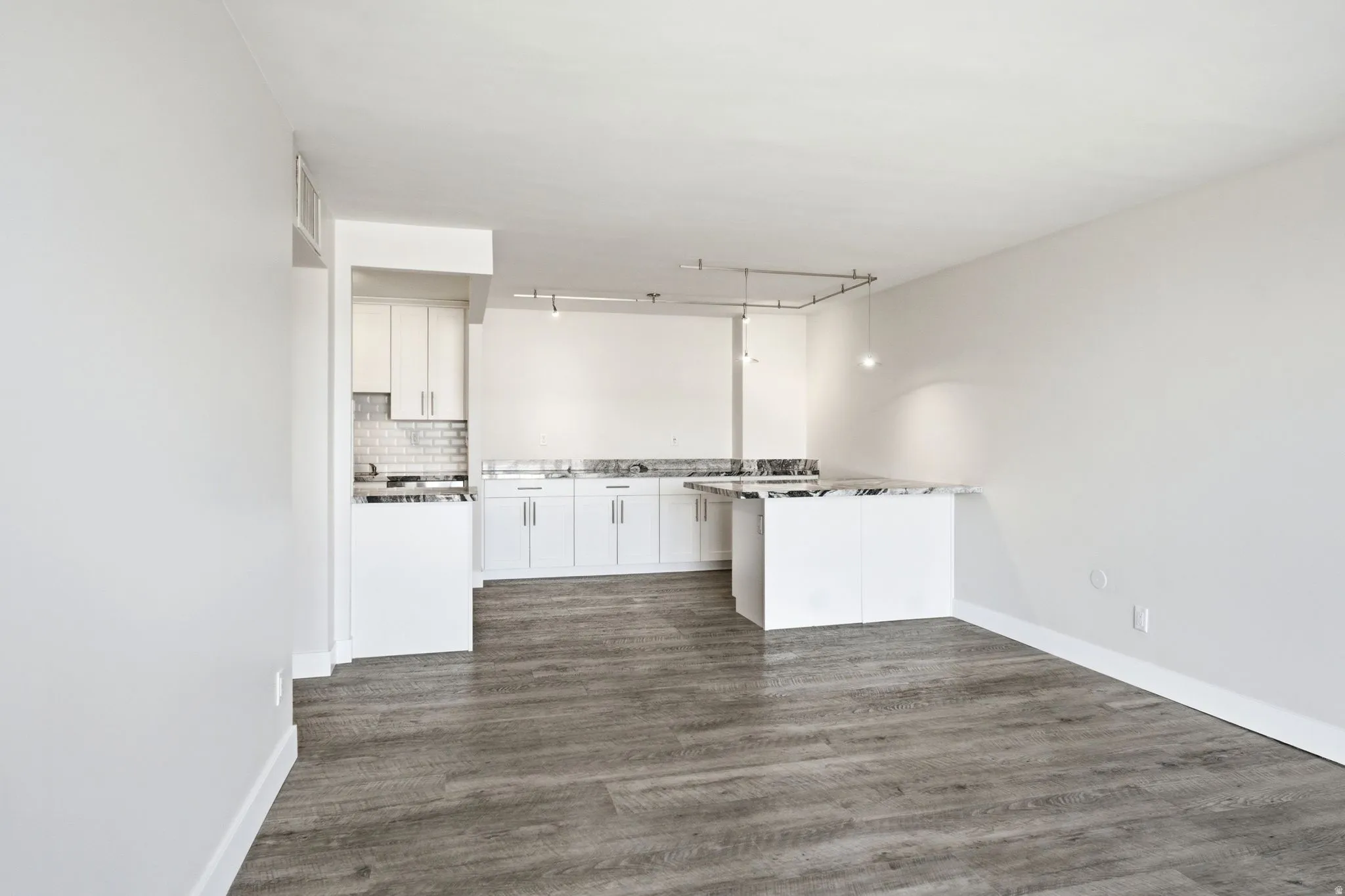 Open-concept space featuring wood-finish flooring, white cabinetry, and light-toned countertops