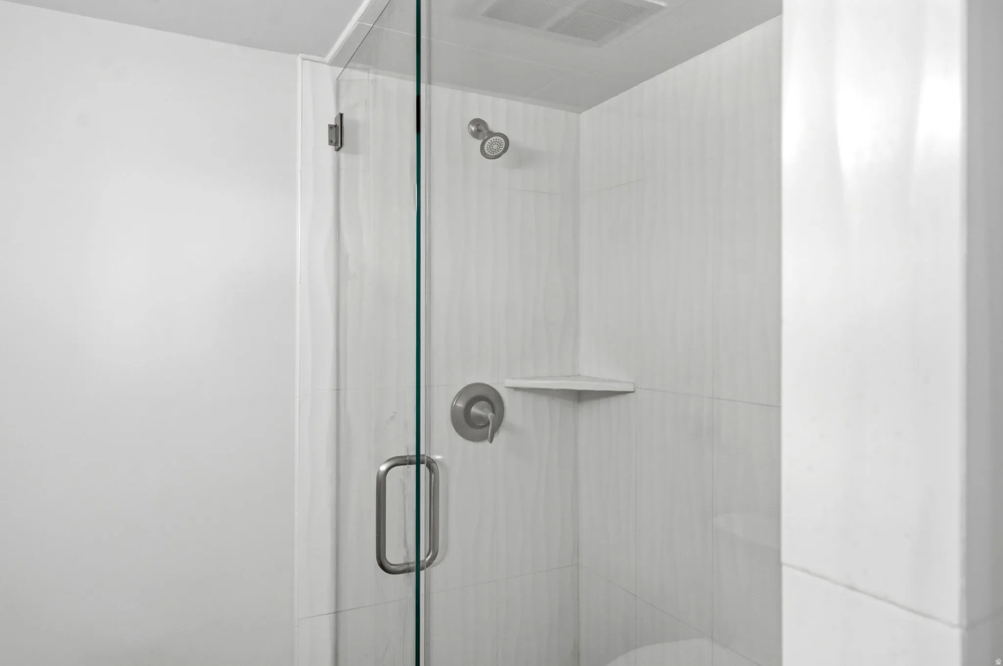 Glass-enclosed shower with a brushed nickel shower head, control handle, and a built-in corner shelf