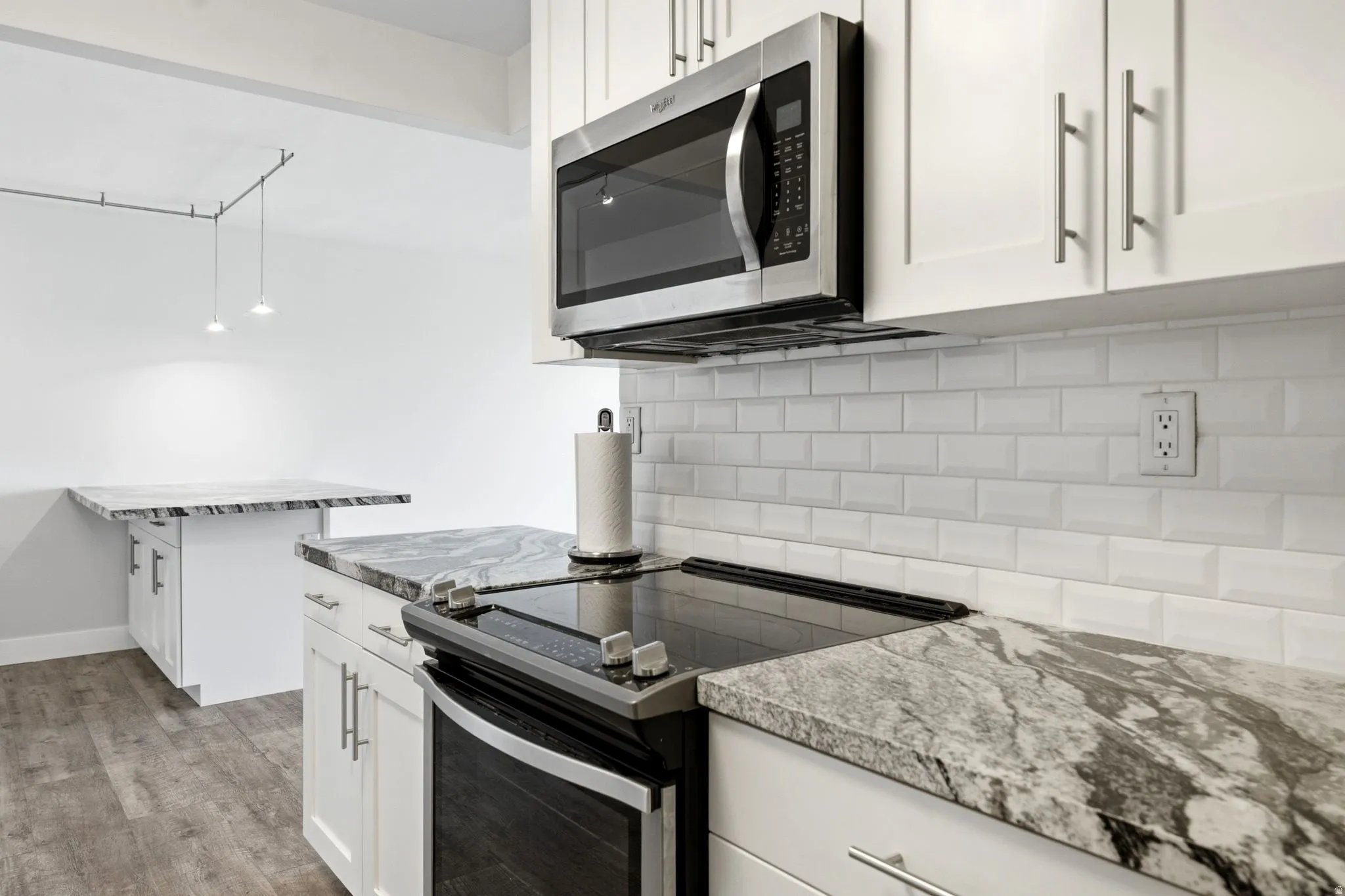 Kitchen featuring white cabinetry, stainless steel microwave, integrated electric cooktop, light-toned countertop with dark veining, and white subway tile backsplash