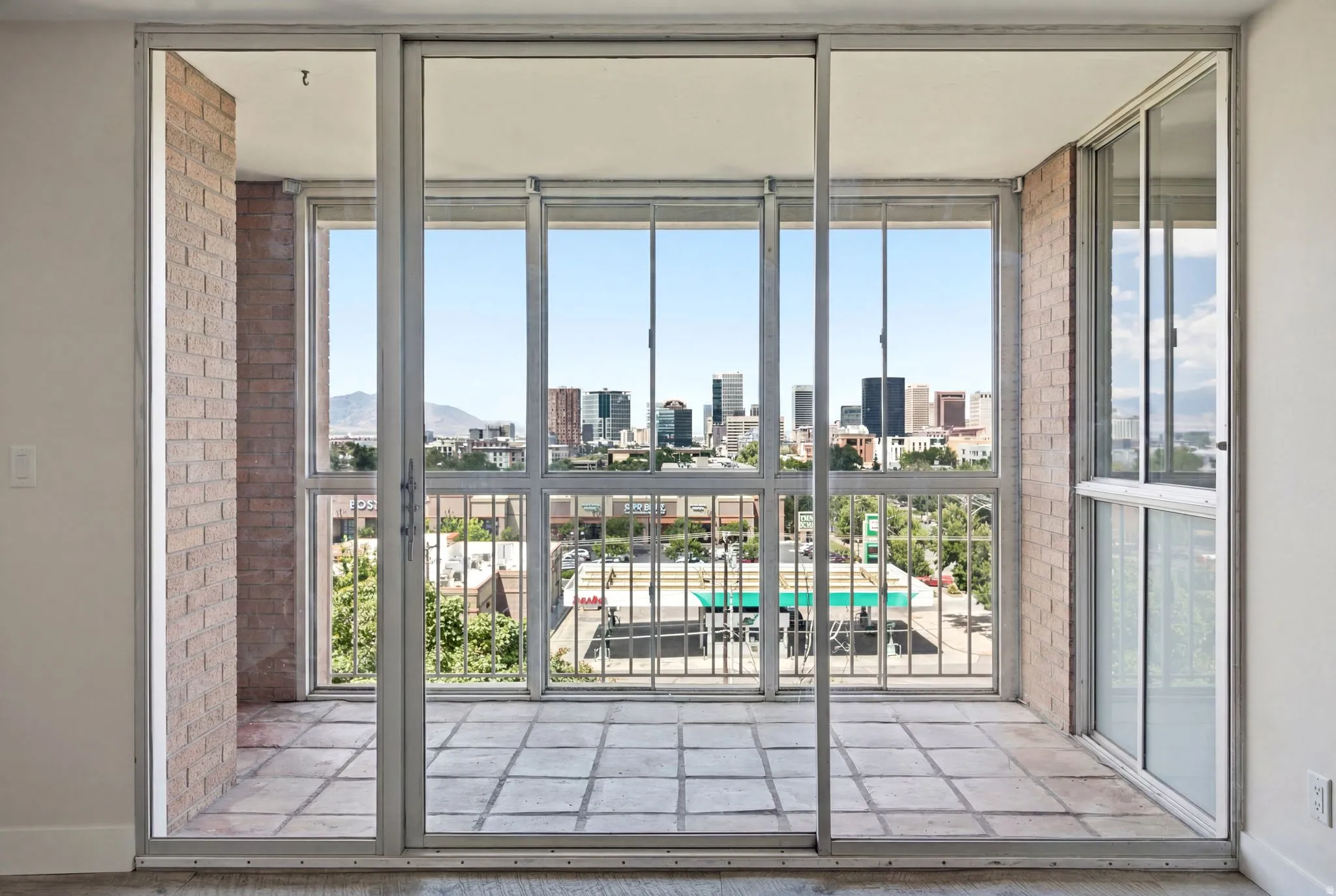 Sliding glass doors opening to an outdoor patio with tiled flooring and a brick-finish wall
