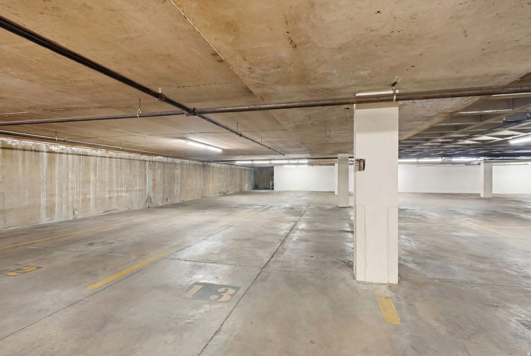 Spacious concrete parking garage with overhead exposed piping and fluorescent lighting
