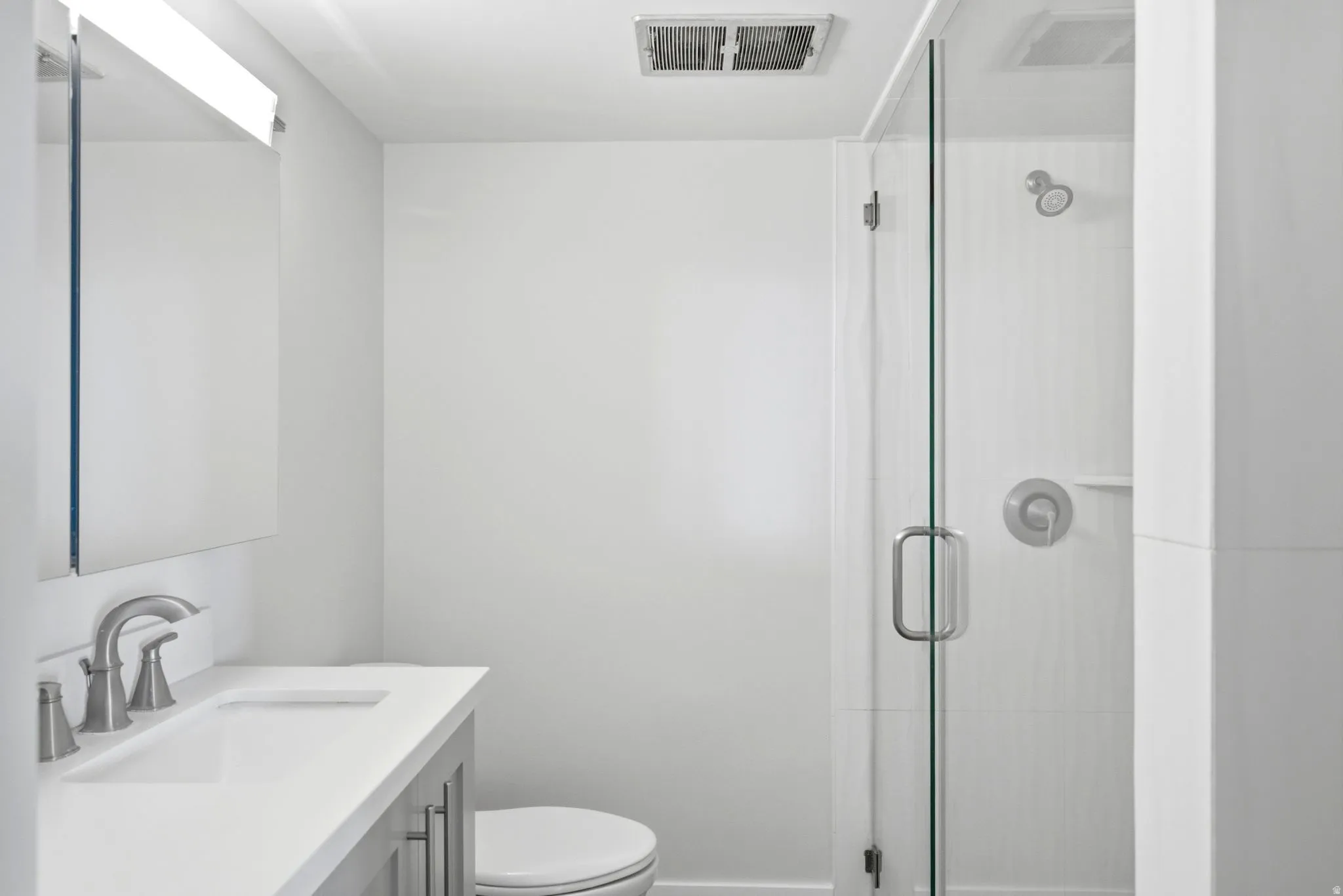 Bathroom featuring a glass-enclosed shower, white tile surround, brushed nickel fixtures, a single vanity with a white countertop, and a wall-mounted mirror