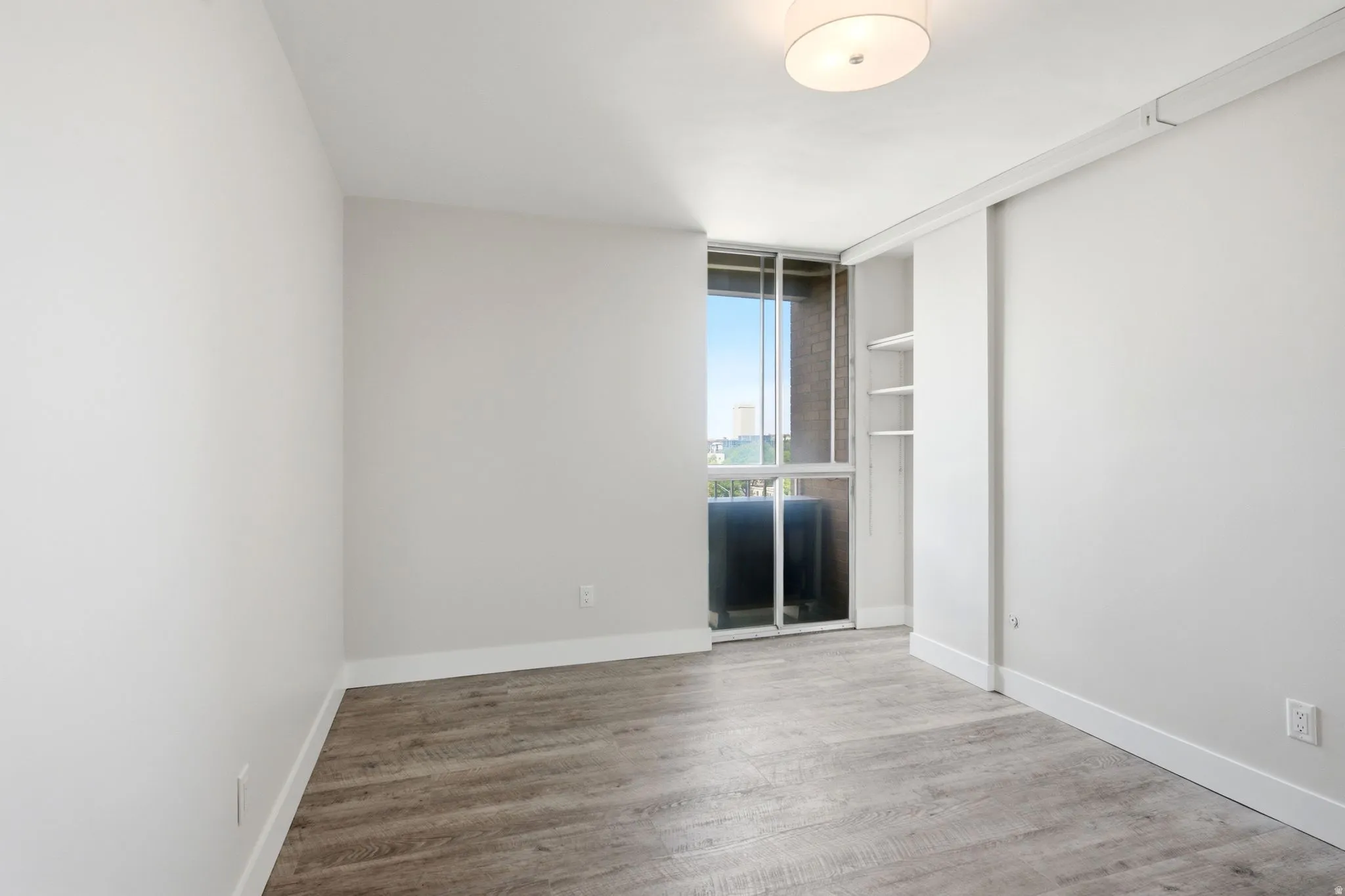 Room featuring wood-finish flooring, a contemporary ceiling light fixture, white baseboards, and a sliding glass door offering access to an exterior space