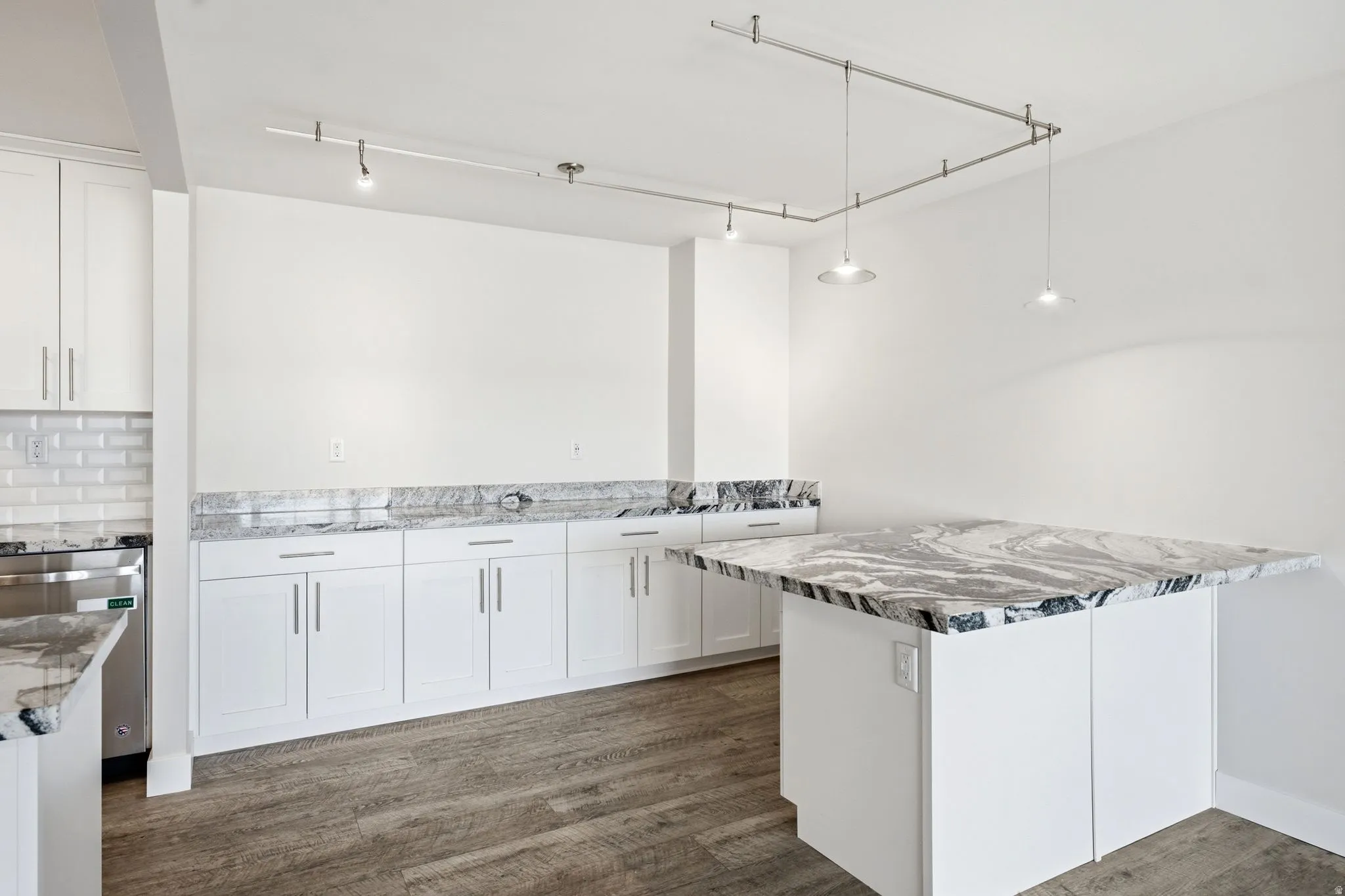 Expansive kitchen featuring a large central island with a waterfall-edge countertop, white shaker-style cabinetry, and wood-finish flooring