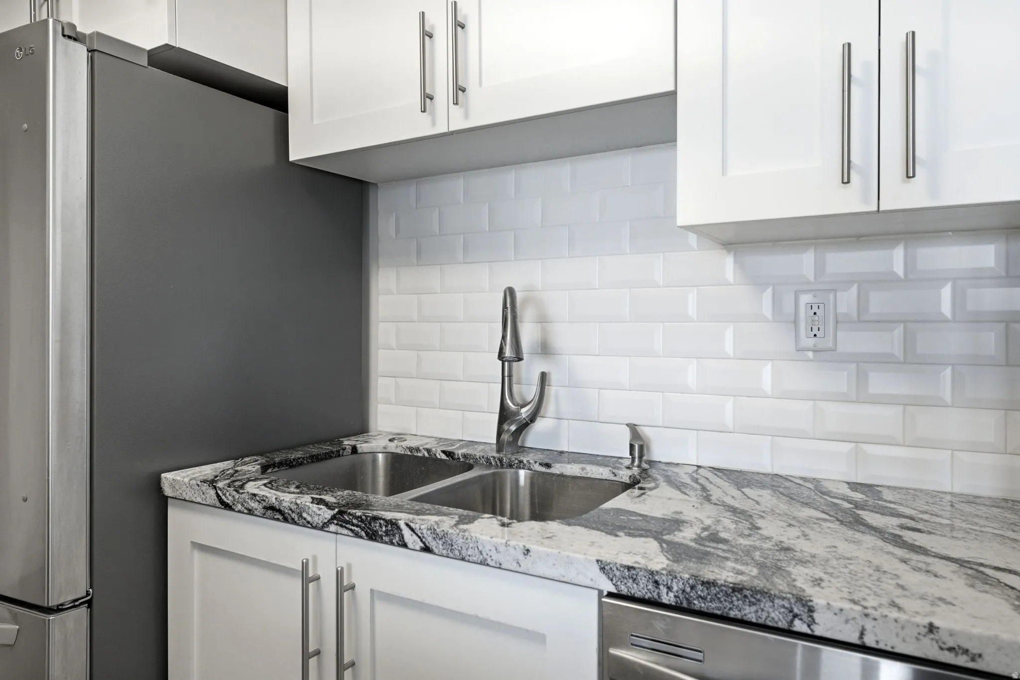 Kitchen featuring white shaker-style cabinetry with brushed nickel hardware, a dual basin stainless steel sink, and a high-arc faucet