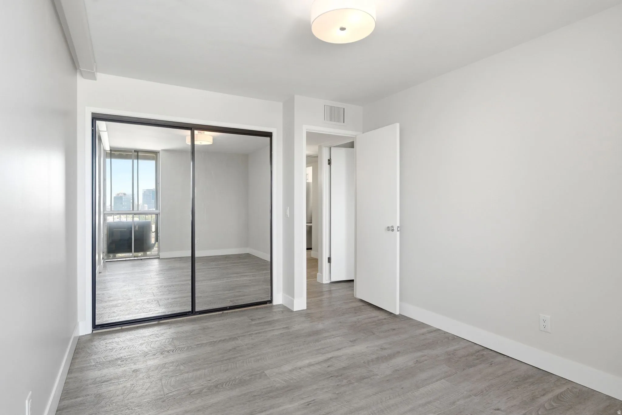 Expansive room featuring wood-finish flooring, light grey walls, white baseboards, and a semi-flush ceiling light fixture