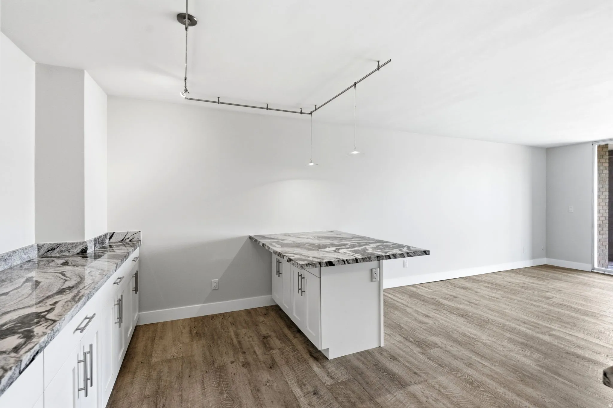 Kitchen area featuring white shaker-style cabinetry with silver-tone hardware, stone countertops with a striking veined pattern, and wood-finish flooring