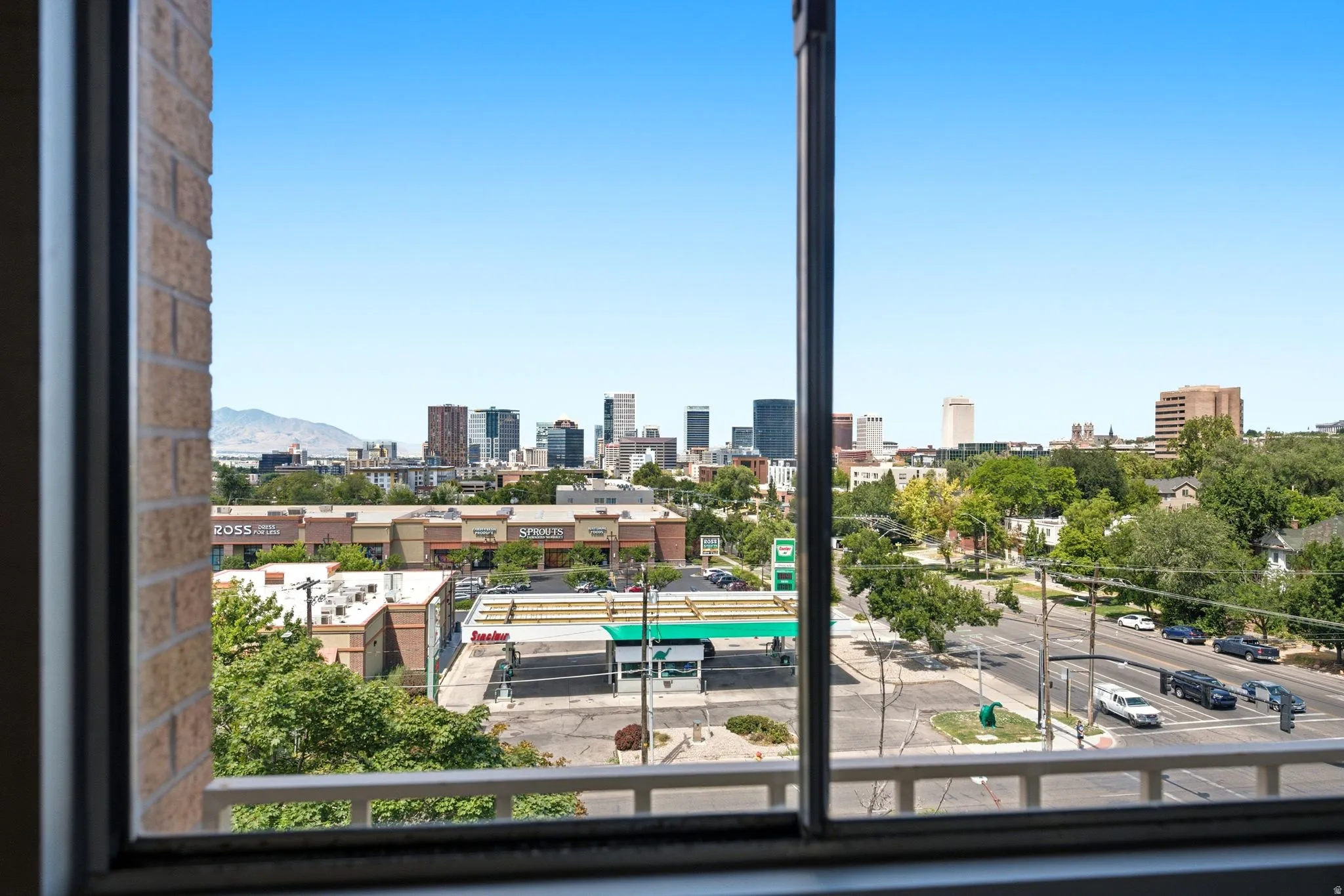 Expansive window framing a skyline with various commercial buildings and distant mountains