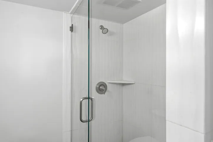 Glass-enclosed shower with a brushed nickel shower head, control handle, and a built-in corner shelf