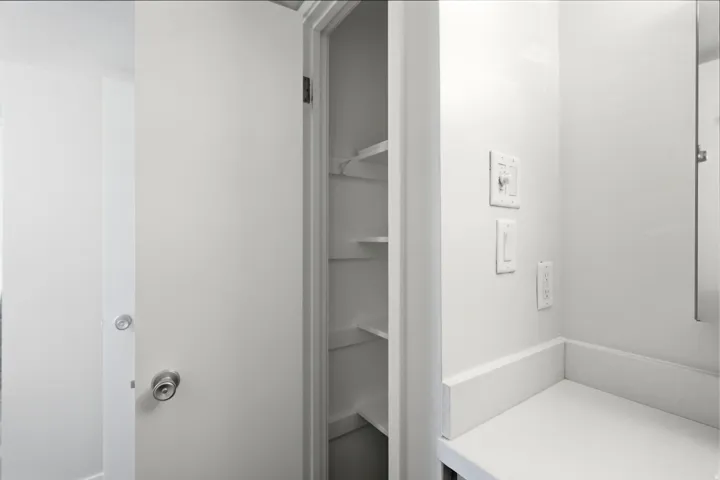 Built-in shelving unit providing storage, complemented by a white countertop, wall-mounted light switches, and a modern door handle
