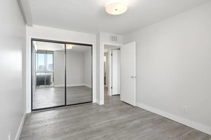 Expansive room featuring wood-finish flooring, light grey walls, white baseboards, and a semi-flush ceiling light fixture