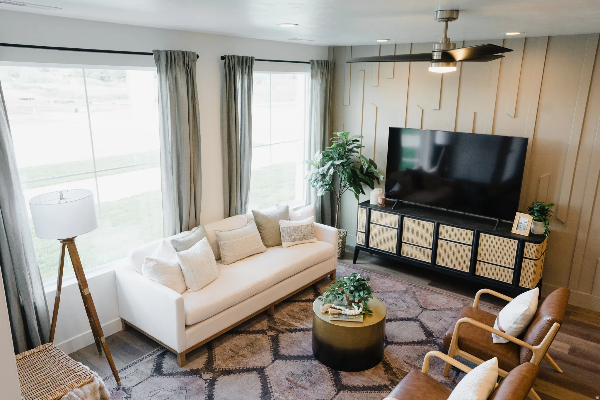 Living area featuring expansive windows with roller shades, wood-finish flooring, and a ceiling fan with integrated lighting