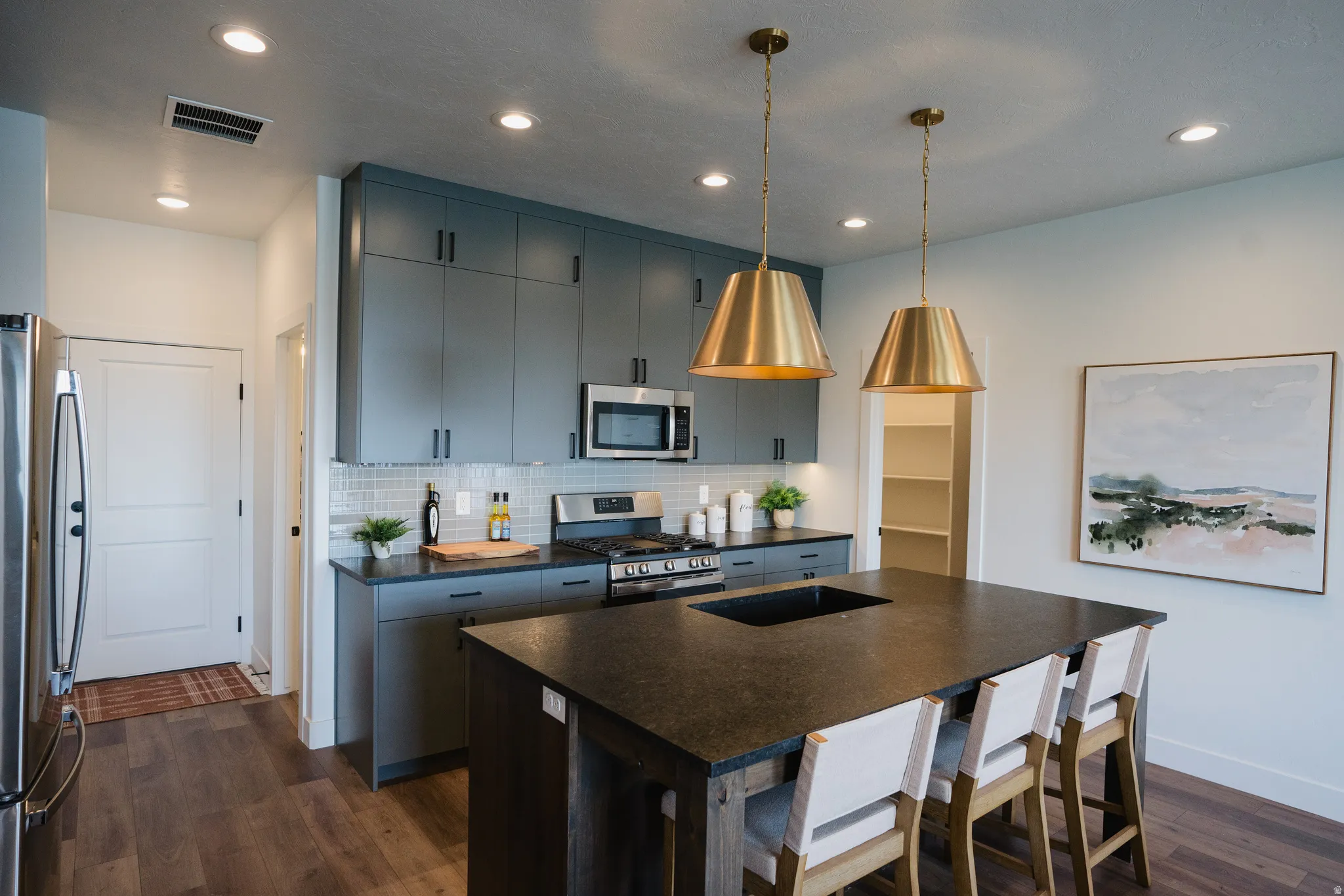 Kitchen featuring a central island with integrated sink, dark countertops, and seating for three