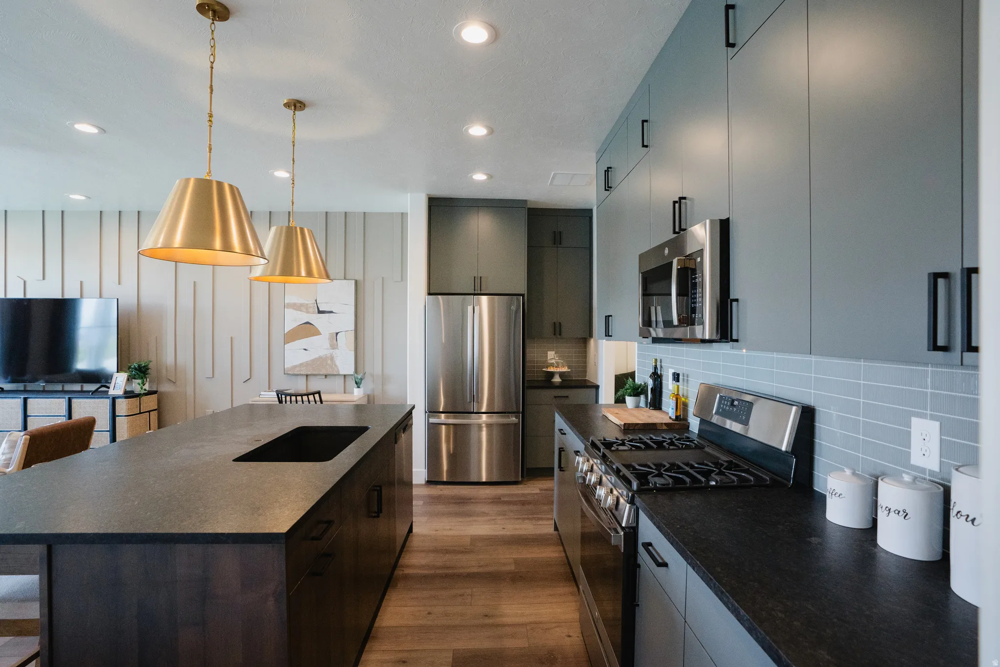 Modern kitchen featuring slate-finished countertops, stainless steel appliances, wood-finish flooring, and shaker-style cabinetry with matte black hardware