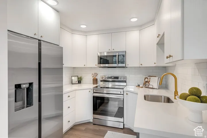 Modern kitchen featuring white cabinetry, stainless steel appliances, a subway tile backsplash, recessed lighting, and wood-finish flooring