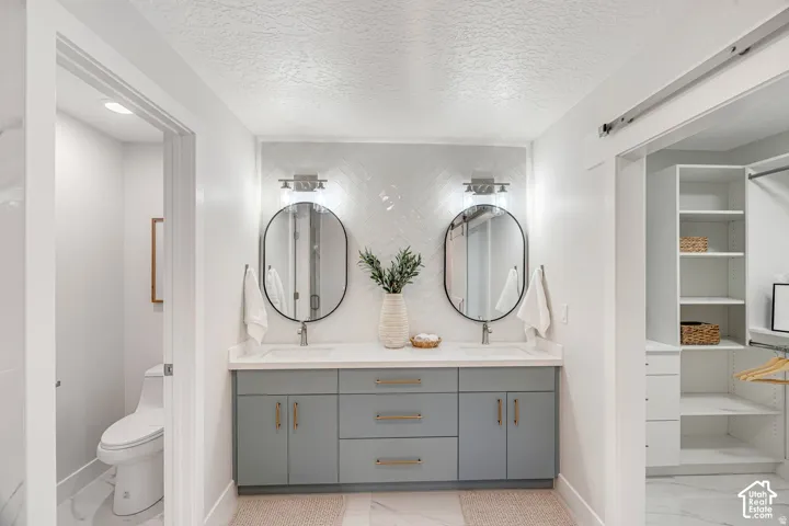Double vanity featuring light grey cabinetry with gold-finish hardware, individual oval mirrors, and wall-mounted light fixtures