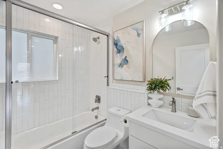 Bathroom featuring a white subway tile shower surround with a glass enclosure, a white vanity with an integrated sink, an arched mirror, and recessed lighting