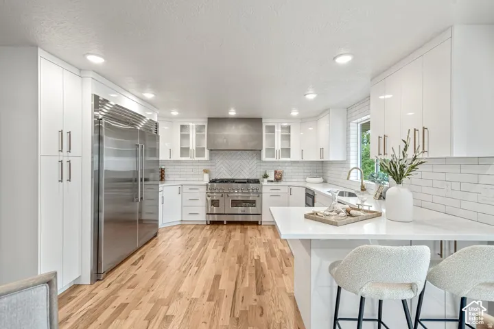 Gourmet kitchen featuring a large stainless steel refrigerator, professional-grade range, white cabinetry, herringbone tile backsplash, and wood-finish flooring