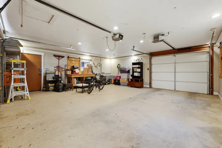 Spacious garage featuring a concrete floor, two overhead garage doors, recessed lighting, and a side access door