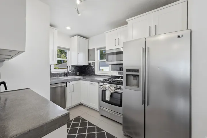 Kitchen featuring white shaker-style cabinetry, stainless steel appliances, dark concrete  countertops, and a decorative mosaic tile backsplash