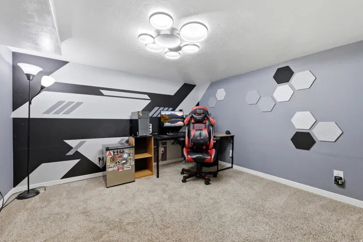 Carpeted room featuring a distinctive black and white geometric accent wall, a contemporary ceiling light fixture with multiple circular elements, and a secondary wall adorned with hexagonal acoustic panels