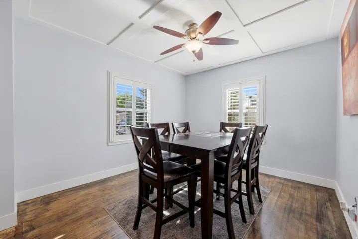 Coffered ceiling with a central ceiling fan, wood-finish flooring, and two windows with white plantation shutters