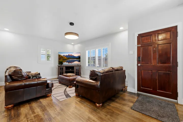 Wood-finish flooring throughout, featuring a paneled wood entry door, white plantation shutters, recessed lighting, and a contemporary ceiling light fixture