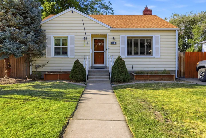 Charming single-story residence featuring light yellow siding, a reddish-brown shingle roof, and a red brick chimney