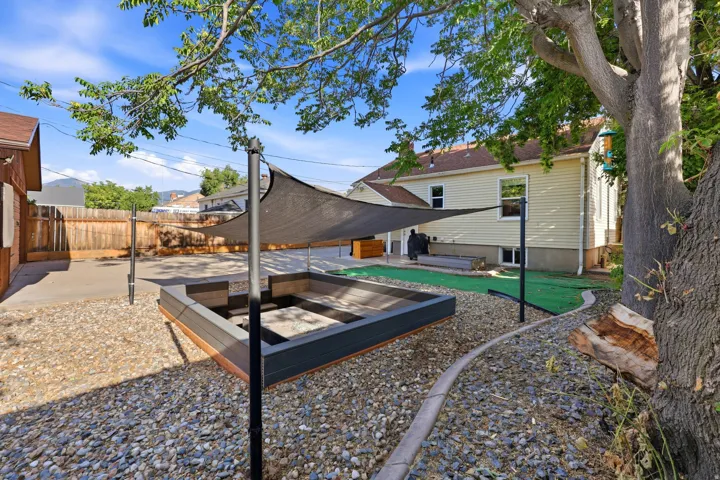 Expansive outdoor space featuring a built-in fire pit, shade sails, gravel landscaping, and a wood privacy fence
