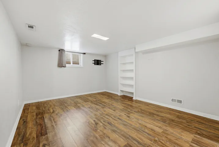 Spacious room featuring wood-finish flooring, white painted walls, and a built-in shelving unit