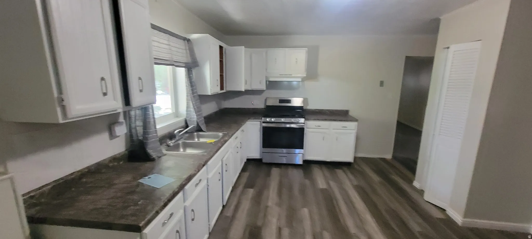 Spacious kitchen featuring white cabinetry, dark countertops, stainless steel range, and wood-finish flooring