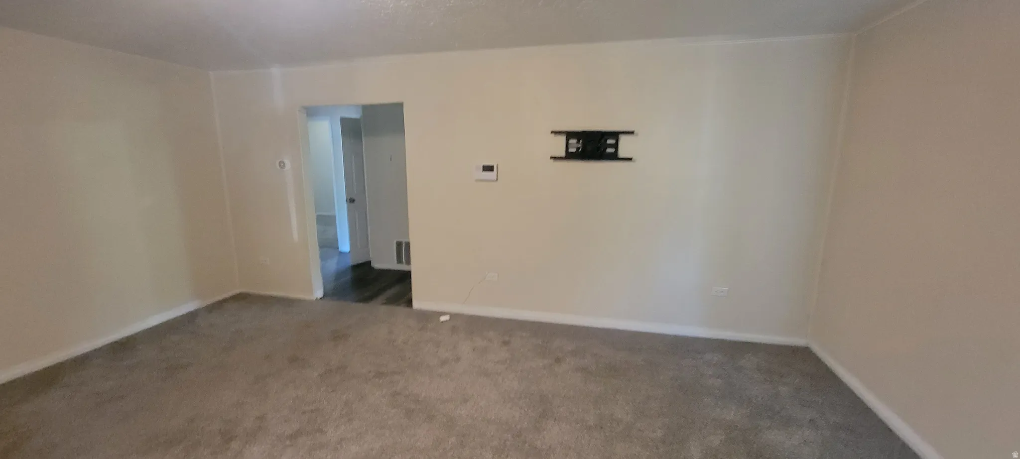Living space featuring neutral wall paint, light-colored carpeting, white trim, and a wall-mounted bracket