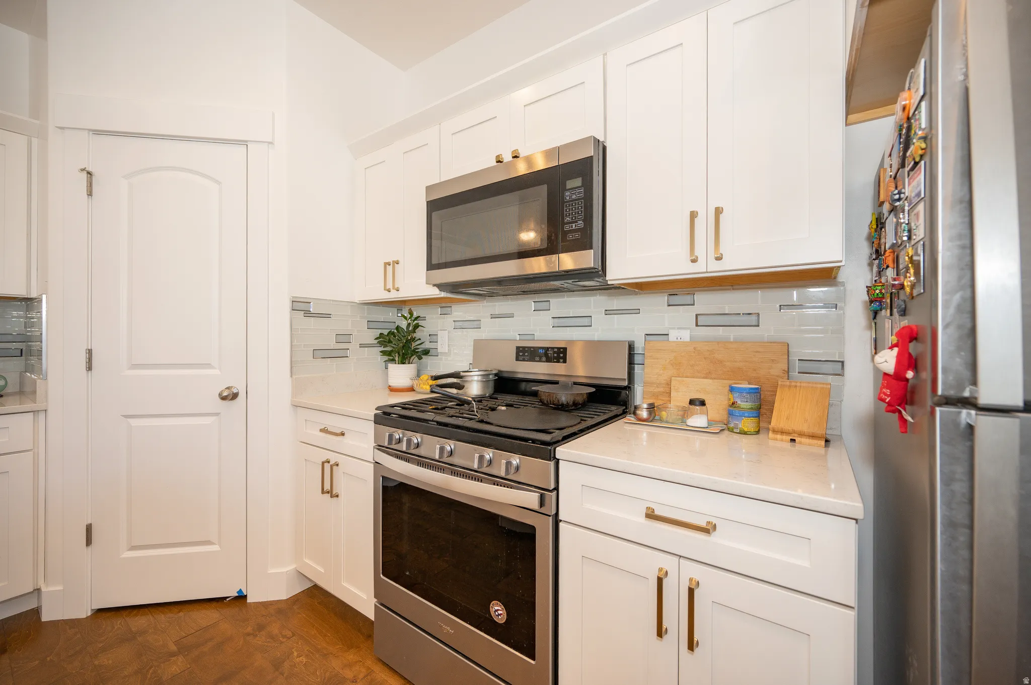 Modern kitchen with white shaker cabinetry, stainless steel appliances, quartz countertops, and a contemporary tile backsplash