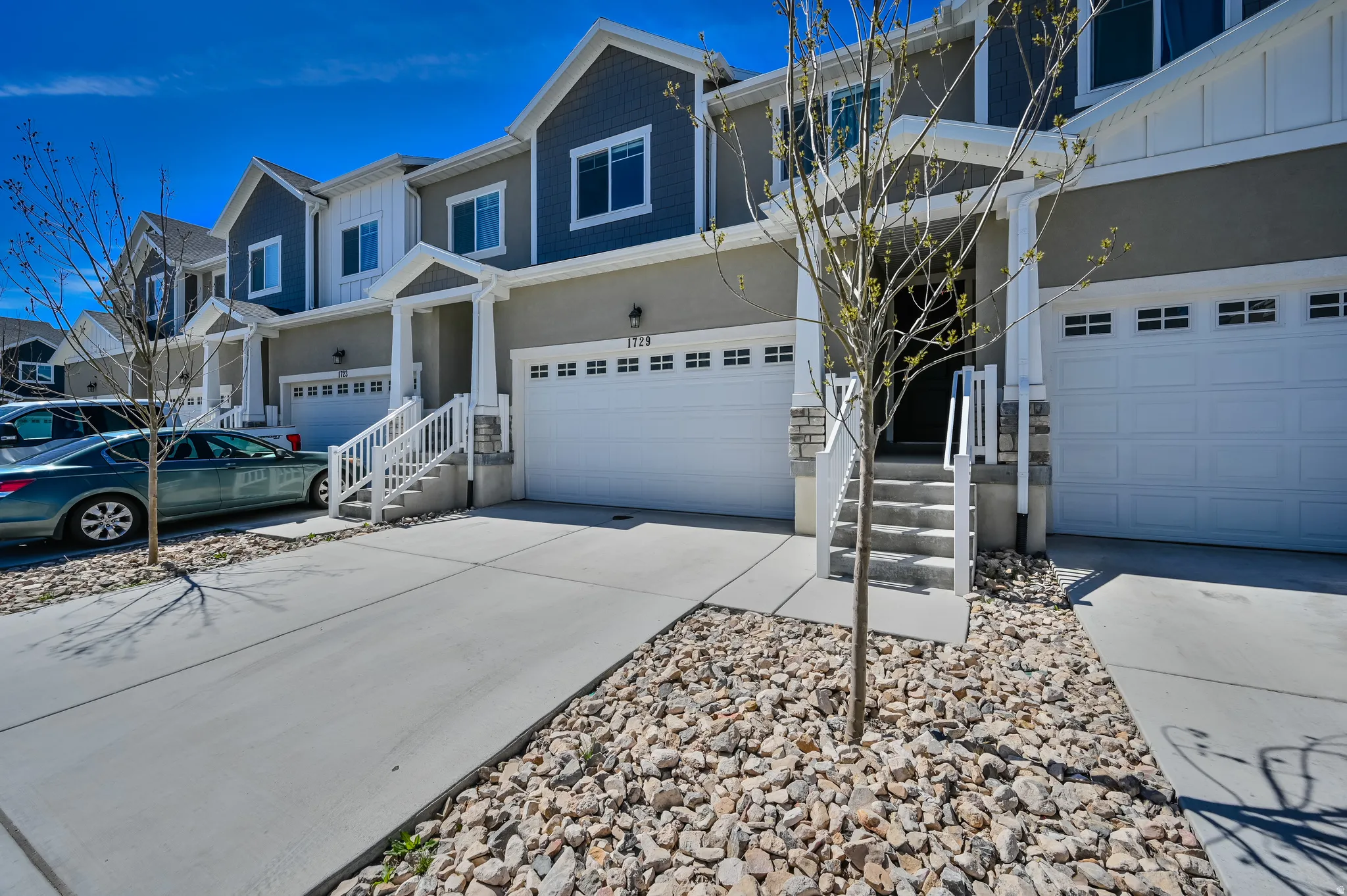 Contemporary townhome exterior featuring a two-car garage, concrete driveway, and rock landscaping