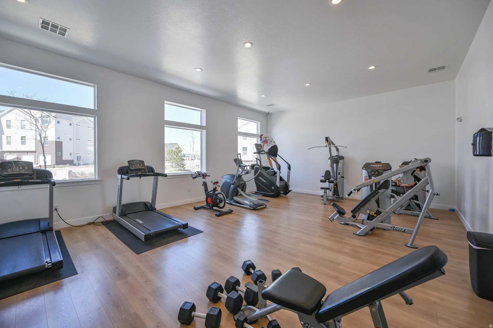Dedicated fitness space featuring wood-finish flooring, ample natural light from multiple windows, recessed ceiling lighting, and crisp white walls