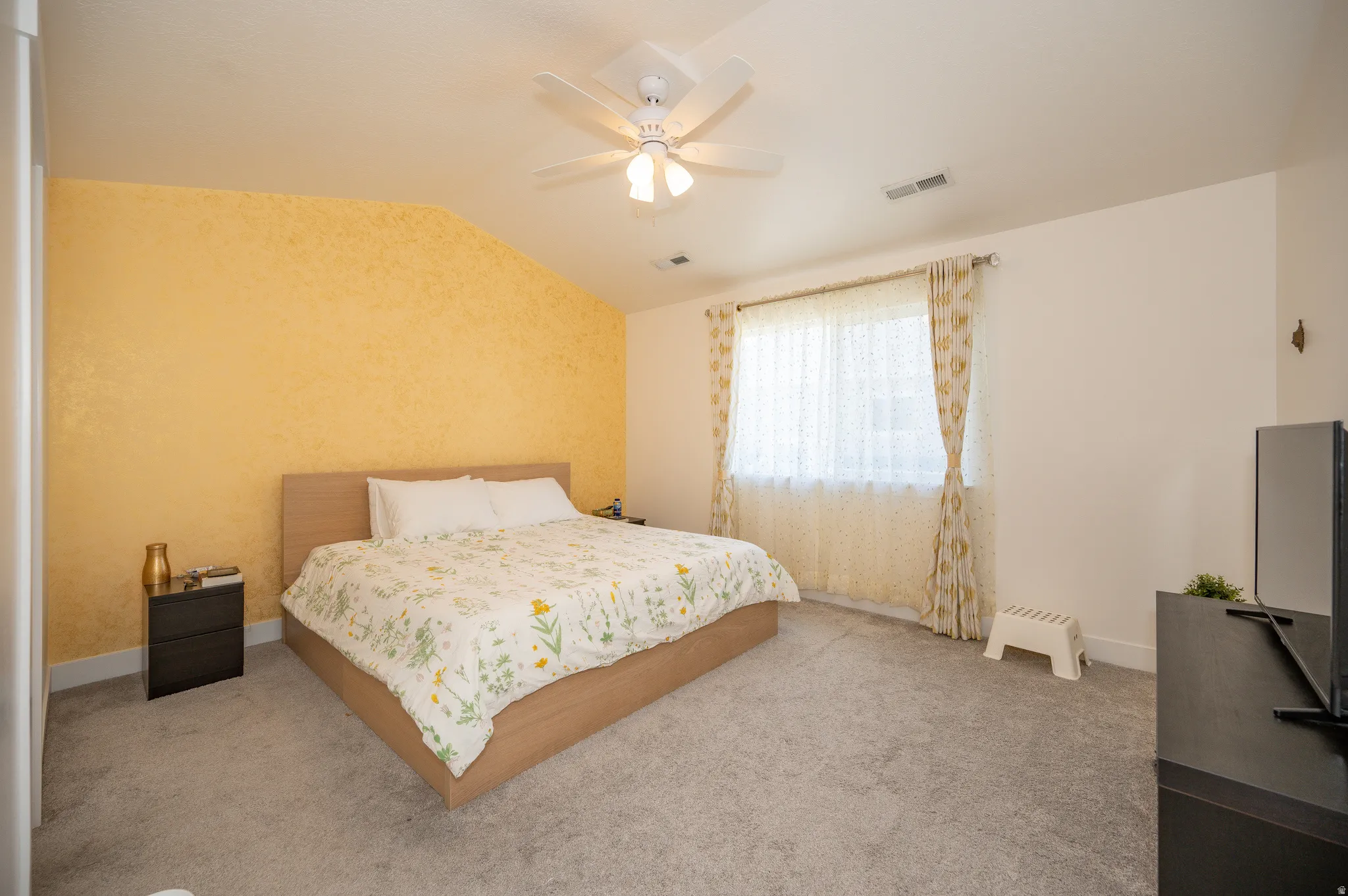 Bright room featuring a textured accent wall, light-colored carpeting, and a ceiling fan with integrated lighting